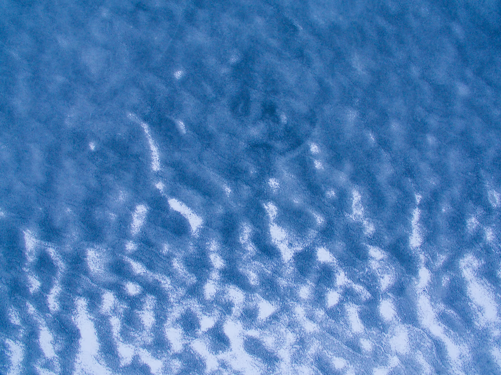 Aerial view of textured sand dunes with shadows creating wave-like patterns.